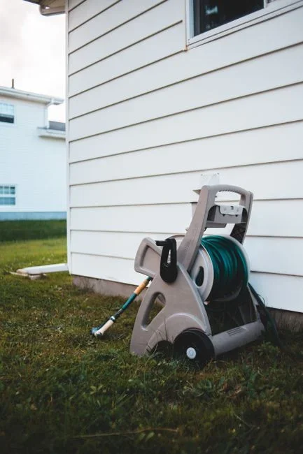 Outdoor hose bib spigot with a garden hose attached and a spray nozzle lying on wet concrete, water seeping from the threaded connection