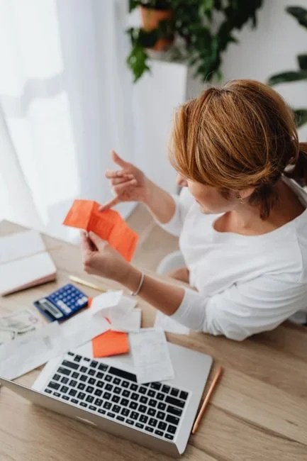 Homeowner at a kitchen table comparing a paper water utility bill against a plumber's itemized repair receipt and a permit copy